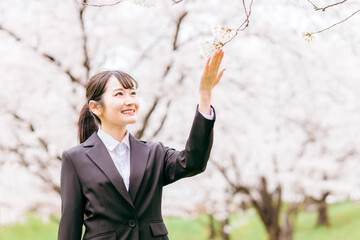 満開の桜の花を見るスーツ姿のビジネスウーマン（フレッシャーズ・新卒・新社会人・就職・入社・新生活）
