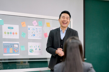 A businessman manager is presenter for explain marketing plan to team in.meeting room by paper chart on board.