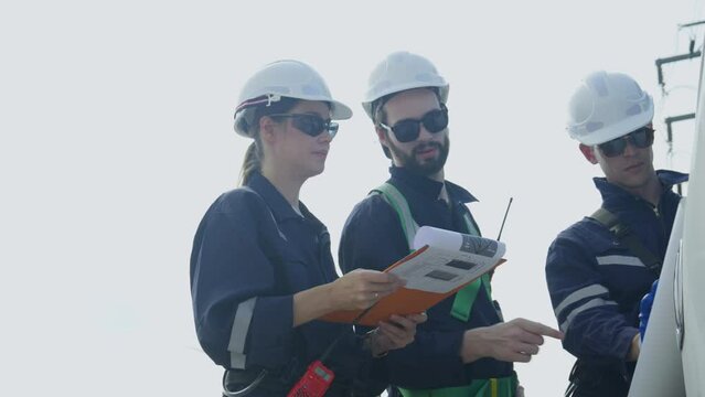 Side view group of technician workers stand beside the van that open the door and discuss about work using plan paper with windmill or wind turbine on the background.