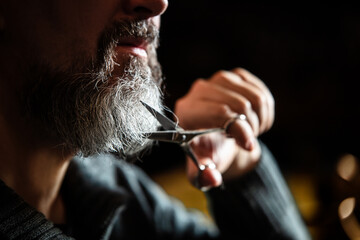 Portrait of a grey bearded man with a scissors, routine treatment for cutting and grooming, closeup
