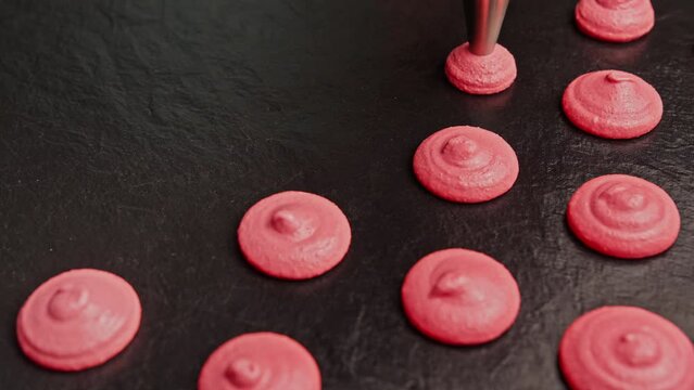Confectioner making macaroons. Extruding pink macaroons from piping bag. Baking concept. Making French dessert. Close-up in 4K, UHD
