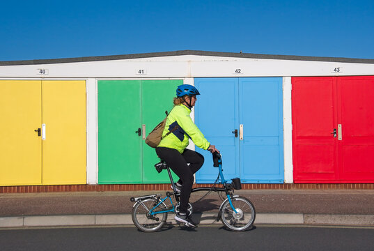Cycling image of a lady on a bicycle riding past a row of brightly coloured beach huts.. Vibrant colours make for a very appealing shot. 