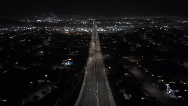 Drone shot of a road with cars driving through illuminated cityscape at night