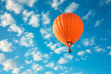 Fototapeta na wymiar a large orange hot air balloon flying through a blue sky with fluffy clouds in the foreground and a blue sky with a few white clouds in the foreground