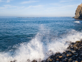Rocky beach with Atlantic Ocean waves meeting with underwater sharp rocks. Blue sea with small waves with foam crashing on the beach, south of Tenerife, Canary Islands