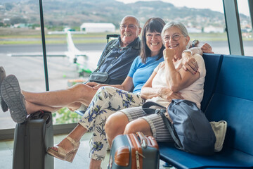 Smiling group of senior friends sitting in airport departure area waiting for boarding. Travel and...