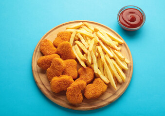 Homemade chicken nuggets and french fries with ketchup on blue background.