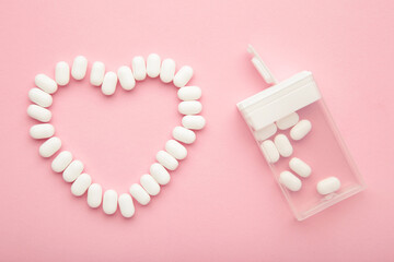 White dragees lie in the shape of a heart on pink background.