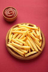 French fries on wooden plate with ketchup in bowl on red background. Vertical photo
