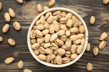 Bowl with pistachios on brown background.