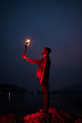 Image of brave man holding burning stick while moving in darkness. Young man holding a fire stick...