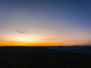 Aerial view A breathtaking sunset paints the sky with vibrant hues of orange and red, .casting a warm glow over the majestic mountains in a tranquil evening landscape.