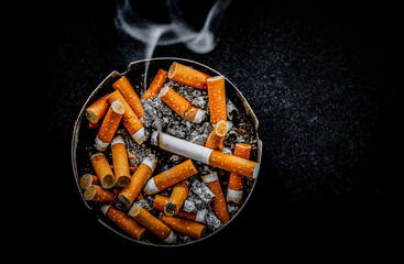 Still life Smoldering cigarette in an ashtray on dark wooden table against black background. Space for text.