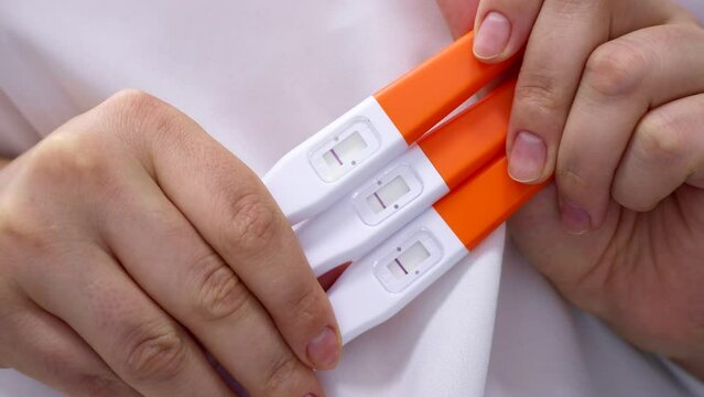 Woman hands holding many pregnancy tests with negative one line result in bathroom. Girl checking plastic test kits at home. Fertility and healthcare concept