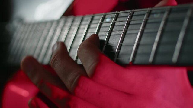 Close-up view of a guitar player masterly moving fingers on a fretboard of on an electric guitar during the performance on a stage with concert light. Musician performing a cheerful song