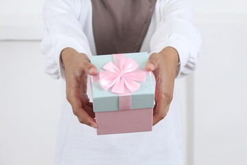 holding out with both hands a pink and blue gift with a pink ribbon