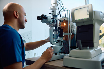Ophthalmologist using optical biometer while checking eyesight of senior patient at clinic.