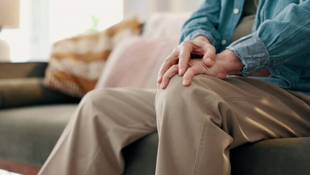 Knee pain, hands and closeup of senior man on a sofa with muscle, cramps or inflammation in his home. Zoom, legs and elderly male person in a living room with arthritis, osteoporosis or fibromyalgia
