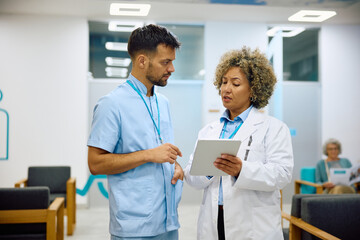 Obraz premium Mature female doctor and medical technician using digital tablet in hallway at clinic.