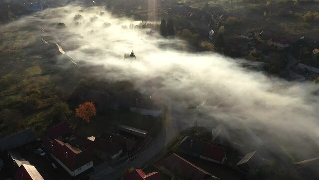 Aerial view of morning mist above a village. House roofs raising from clouds by drone