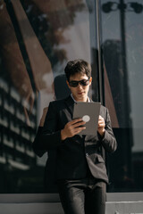 Asian male businessman use smartphone and holding laptop computer, Walk enjoy smiling while doing commuting at business center.