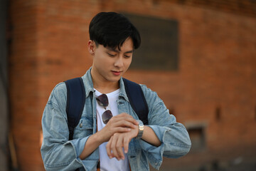 A backpacked male tourist checking the time on his wristwatch, standing at the Tha Phae gate,...