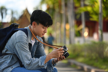 The young Asian man who is a photographer looking at a photograph from a photo session while resting from traveling Thai temple