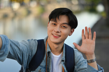 Handsome young Asian traveler smiling and waving at mobile camera, Travel Influencer and Solo traveler concept