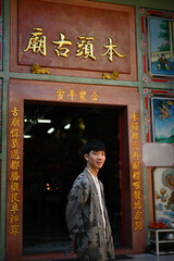 Obraz premium Vertical image and Portrait of a happy young Asian man wearing a robe standing in front of the entrance to a Chinese shrine