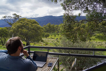 Fototapeta premium A man working remotely from his balcony looking over bushland and mountains