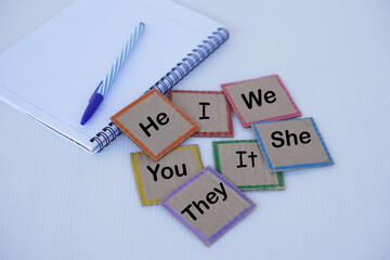 Square paper cards with pronouns word He She It  I You We They. Paper notebook and pen. Concept,...
