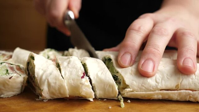 A pita roll is cut into pieces with a knife. Preparation of a roll with cheese, fish and vegetables