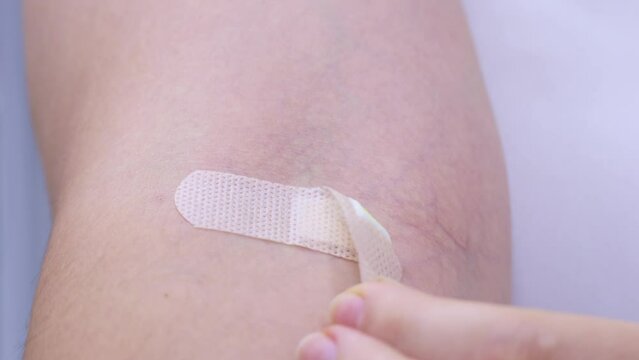 Hand removing beige adhesive bandage or medical sticking plaster for first aid from the arm with injection mark close up