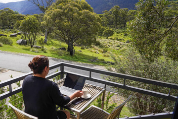 Fototapeta premium A woman working remotely from her balcony looking over bushland and mountains