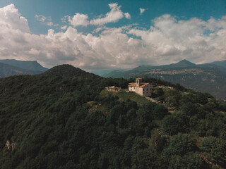 Fototapeta na wymiar aerial view with drone of a naturalistic mountain landscape with an ancient abandoned church on top. The structure is surrounded by greenery and the day is clear and sunny during the summer period