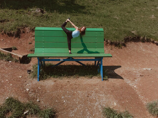 Aoung Caucasian girl with blonde curly hair performs an athletic yoga pose while standing on a...