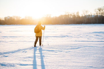 Skiing on a frozen lake, a person moving on cross-country skis in the snow, a beautiful evening sunset in winter, outdoor activities.