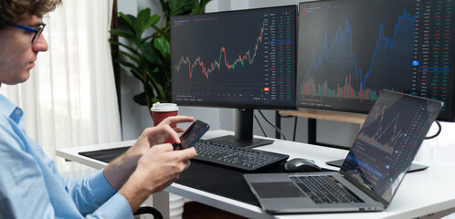 Young investor in stock trader looking on smartphone of dynamic financial exchange investment surrounded current market graph screen in real time at modern office, analyzing statistic profit. Gusher. - obrazy, fototapety, plakaty