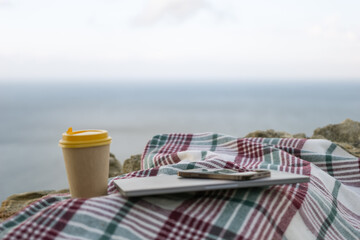 Laptop coffee on blanket with ocean view. Illustrating serene outdoor laptop use. Freelancer enjoying their time outdoors while working or browsing the internet.
