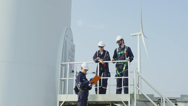 One professional technican worker give the document to her coworker walk to base area of windmill or wind turbine.
