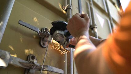 Close-up of a hand with a tool opening the lock of a large container, sparks flying. A cutting worker opens a large iron container. Container for transporting goods.