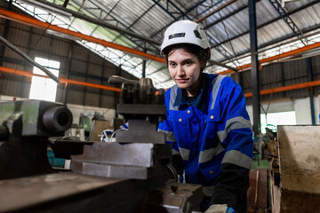 Fototapeta na wymiar Asian female workers wearing uniform safety and hardhat working an iron cutting machine in factory Industrial. Engineering worker man work machine lathe metal. Heavy industry concept.