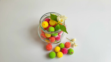 Multicolored candies with chubushnik flowers in a jar on a table on a white background