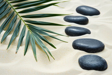 Obraz na płótnie Canvas Black stones and palm leaves on white sand, beautiful sand texture for background. Spa background. Top view.