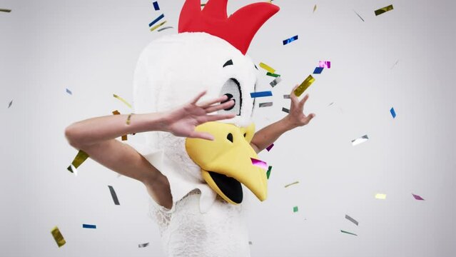 Confetti, dance and chicken costume with woman in studio on gray background for wedding or party. Comic, energy and celebration with person in mask for disco, function or ceremony of tradition