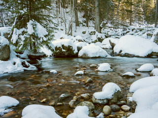 Long exposure photo of a mountain stream in winter, huge boulders and rocks with a thick layer of snow.
