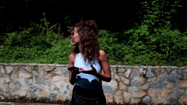 Young Caucasian girl finds herself alone and lost in a naturalistic location. The girl performs typical Italian broad gestures while she checks the direction on her smartphone