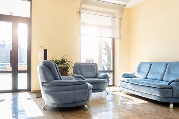 Sunlit, cozy lounge corner featuring plush blue armchairs and a matching sofa, with a tranquil view through large windows, perfect for relaxation or casual meetings
