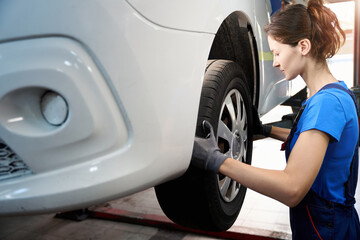 Woman auto mechanic inspects the front wheel of a car