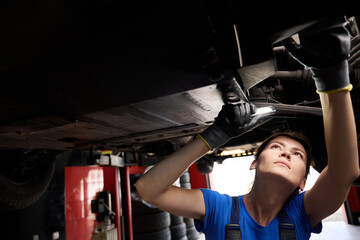 Young repair technician inspecting the underbody of a car